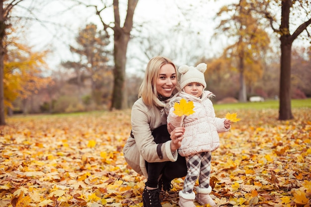 Jeune mère et petite fille marchent à l'automne. Maman et fille jouent. Hiver chaud. Automne lumineux. Confortable.