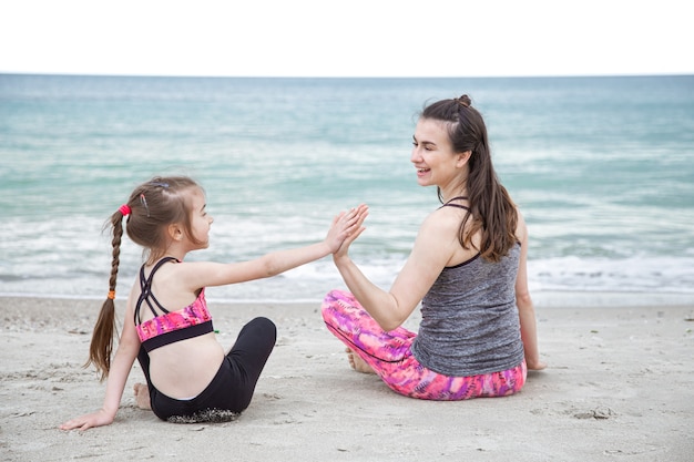 jeune mère avec une petite fille en tenue de sport sont assis sur la plage dans le contexte de la mer. Des valeurs familiales et un mode de vie sain.