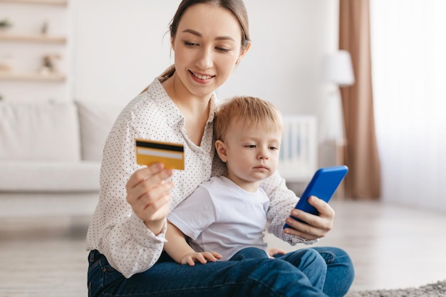 Jeune mère positive et adorable petit garçon faisant des achats en ligne ensemble tenant une carte de crédit et