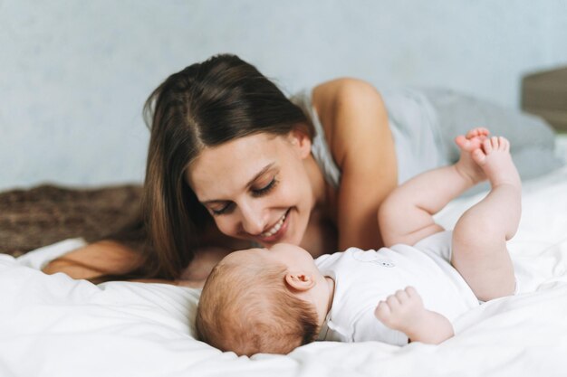 Jeune mère s'amusant avec une jolie petite fille sur le lit avec des tons naturels de lin blanc aime l'émotion