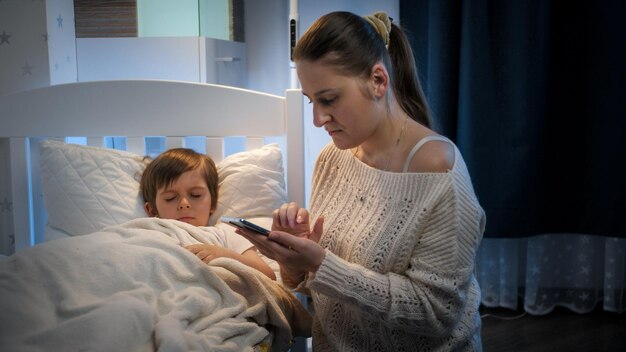 Photo jeune mère s'inquiétant de son fils malade dormant au lit appelant le médecin concept de maladie des enfants