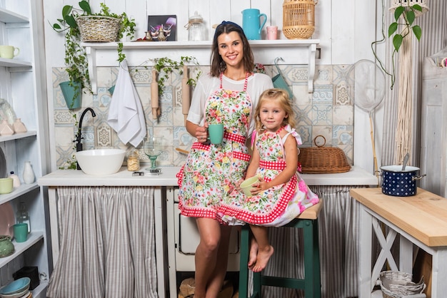 Jeune mère et sa fille cuisinent dans la cuisine dans de beaux tabliers