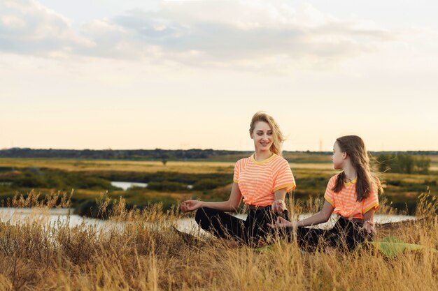 Jeune mère avec sa fille dans les mêmes vêtements faisant du yoga en plein air