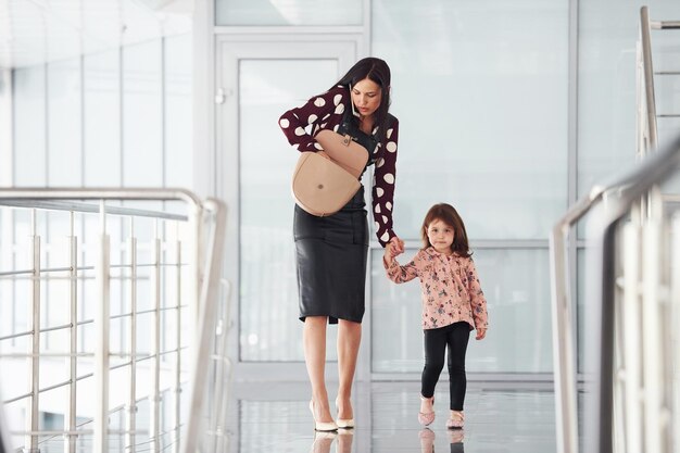 Jeune mère avec sa fille marchant ensemble à l'intérieur au bureau ou à l'aéroport En vacances