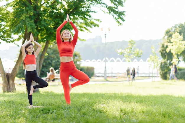 Une jeune mère et sa fille en tenue de sport font du yoga ensemble dans un parc
