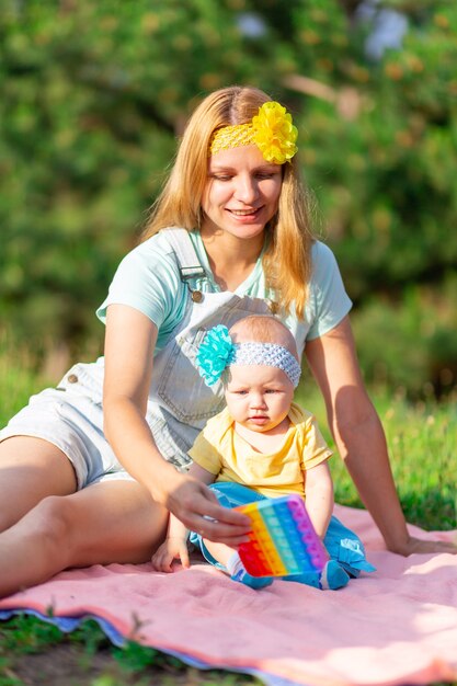 Une jeune mère et sa fille vêtues de vêtements décontractés brillants s'assoient sur la pelouse et jouent avec des bulles éternelles