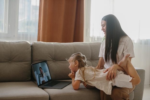 Une jeune mère et sa petite fille consultent leur médecin de famille en ligne à l'aide d'un ordinateur portable