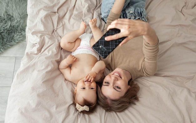 Jeune mère avec sa petite fille fait selfie en position allongée sur le lit Concept de famille heureuse