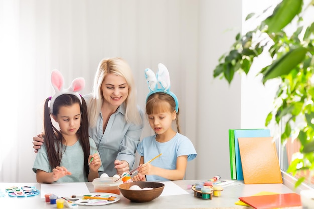 Jeune mère et ses deux petites filles peignant des œufs de Pâques colorés à la maison