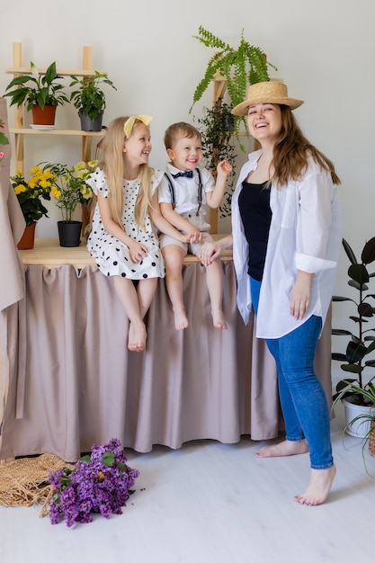 jeune mère avec son fils et sa fille rit des câlins et joue à l'intérieur avec des fleurs à la maison