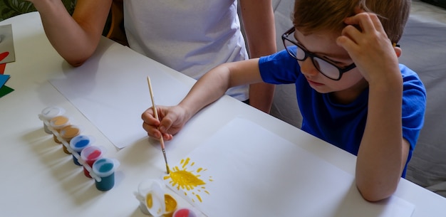 Une jeune mère et son mignon petit fils dans des verres dessinent ensemble avec des peintures sur papier blanc.