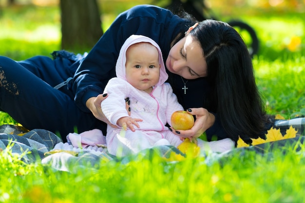 Jeune mère avec son petit bébé dans un parc assis sur un tapis sur l'herbe verte luxuriante offrant à l'enfant une pomme d'automne fraîche