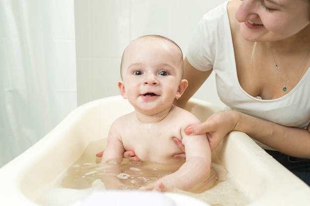 Jeune mère souriante lavant son bébé mignon dans un bain en plastique