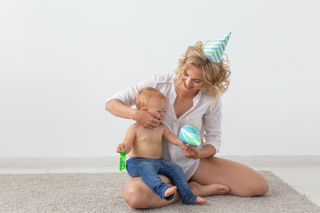 Jeune mère souriante et mignonne petite fille en casquettes d'anniversaire passer du temps ensemble sur un tapis à