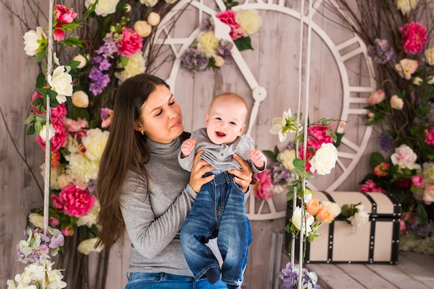 Jeune mère tenant son nouveau-né. Maman allaite bébé. Femme et nouveau-né dans une chambre blanche avec fauteuil à bascule et berceau bleu. Intérieur de la pépinière. Mère jouant avec un enfant qui rit. Famille à la maison