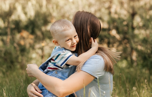 Une jeune mère tient dans ses bras et embrasse un petit garçon en été dans la nature