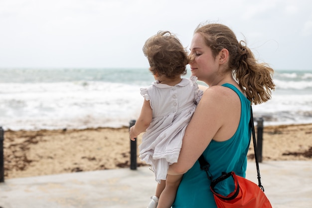 Une jeune mère tient doucement avec amour une petite fille dans ses bras sur fond de mer.