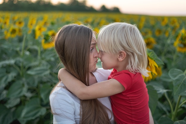 Jeune mère tient son fils dans ses bras sur fond de champ de tournesol. Mère et fils se frottent le nez drôle