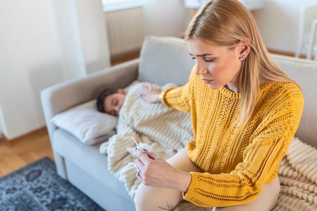 Jeune mère touchant la tête de son fils mesurant la température, le rhume ou la grippe, la fièvre de la maladie, regardant le thermomètre, la toux et la douleur à la gorge, petit enfant, soins maternels