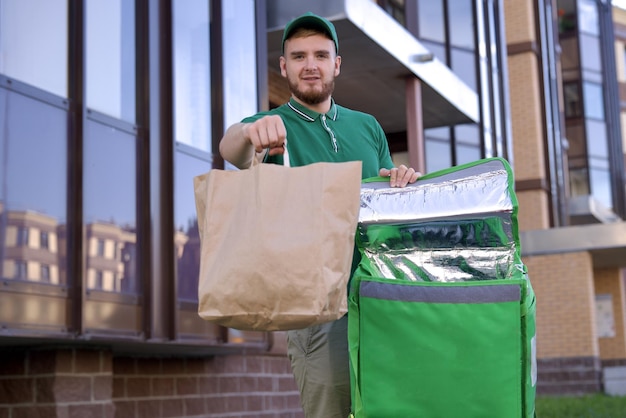Un jeune messager heureux en uniforme vert avec un gros sac thermo ou un sac à dos livre de la nourriture de