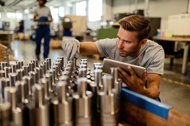 Photo jeune métallurgiste utilisant un pavé tactile lors de l'examen de tiges d'acier dans une usine avant la distribution