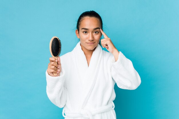 Jeune métis indien tenant une brosse à cheveux pointant sa tempe avec le doigt, pensant, concentré sur une tâche.