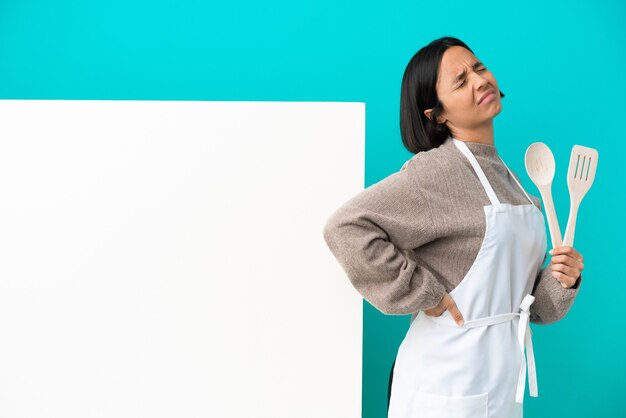 Jeune métisse cuisinier femme avec une grande pancarte isolée sur mur bleu souffrant de maux de dos pour avoir fait un effort