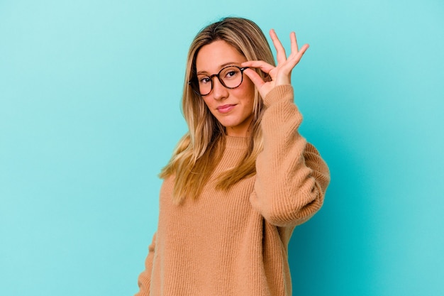 Jeune métisse femme isolée sur bleu excité en gardant le geste ok sur les yeux.