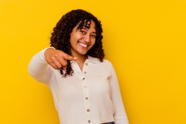 Photo jeune métisse femme isolée sur fond jaune sourires joyeux pointant vers l'avant.