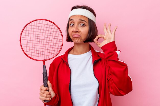 Jeune métisse femme jouant au badminton isolé sur mur rose joyeux et confiant montrant le geste ok.