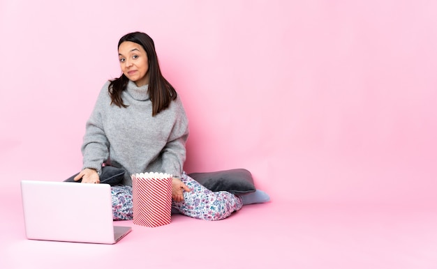 Jeune métisse femme mangeant du pop-corn tout en regardant un film sur l'ordinateur portable heureux et souriant