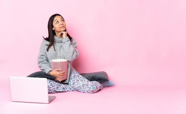 Jeune métisse femme mangeant du pop-corn tout en regardant un film sur l'ordinateur portable