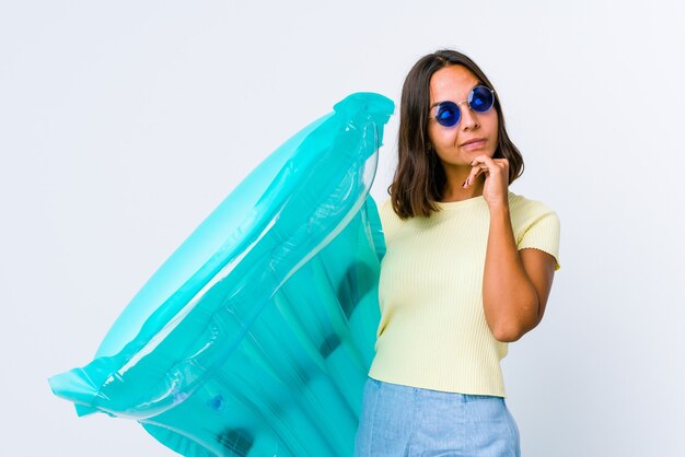 Jeune métisse femme tenant un matelas pneumatique en pensant à quelque chose à un espace de copie.