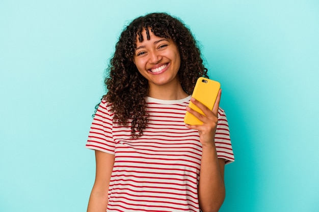 Jeune métisse femme tenant un téléphone mobile isolé sur un mur bleu heureux, souriant et joyeux.