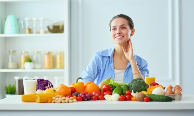 Jeune et mignonne femme assise à la table pleine de fruits et légumes à l'intérieur en bois