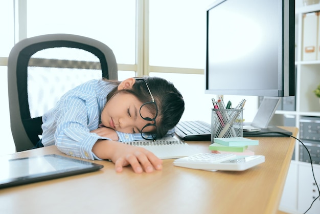 jeune mignonne petite femme employée de bureau travaillant sur ordinateur depuis longtemps se sentant fatiguée et allongée sur le bureau en train de dormir au repos.