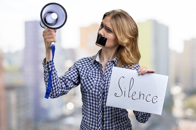 Jeune militante tenant un mégaphone et une bannière avec inscription Silence.