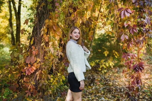 Jeune et mince femme vêtue d'une robe noire et d'une veste de fourrure posant dans un parc d'automne