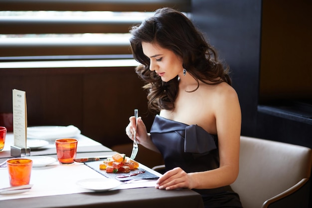 Jeune modèle attrayant avec des cheveux et du maquillage arrangés portant une robe élégante servant un dessert au restaurant