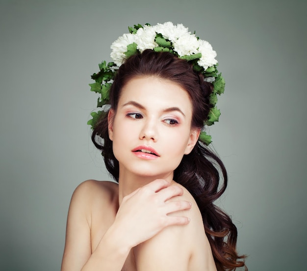 Jeune modèle féminin avec des fleurs blanches et des feuilles vertes sur les cheveux