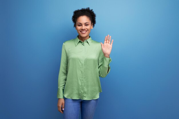 Un jeune modèle féminin positif aux cheveux noirs bouclés vêtu d'un chemisier vert et d'un jean sourit