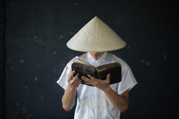 Jeune moine asiatique au chapeau sur fond de mur noir