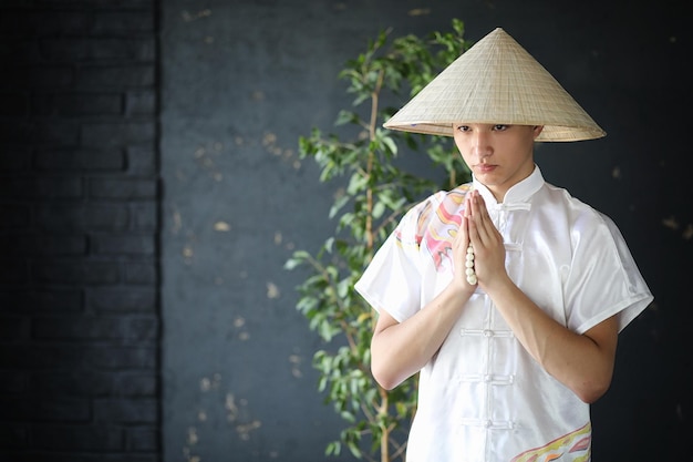 Jeune moine asiatique au chapeau sur fond de mur noir