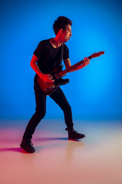 Jeune musicien caucasien jouant de la guitare à la lumière néon sur fond bleu, inspiré