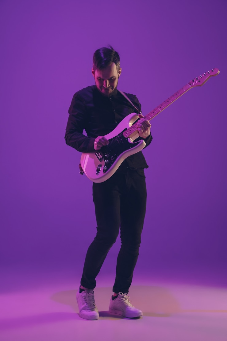 Photo jeune musicien caucasien jouant de la guitare en néon sur fond violet
