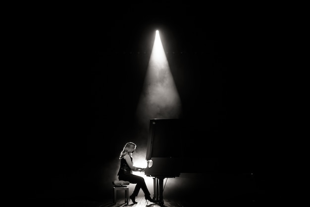 Jeune musicien jouant du piano à queue sur la scène dans le faisceau de lumière