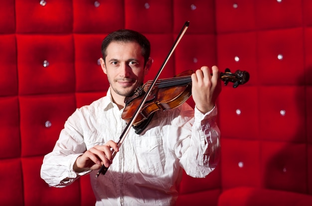 Jeune musicien jouant du violon dans un restaurant sur un mur rouge.