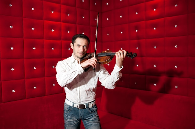 Jeune musicien jouant du violon dans un restaurant sur un mur rouge.