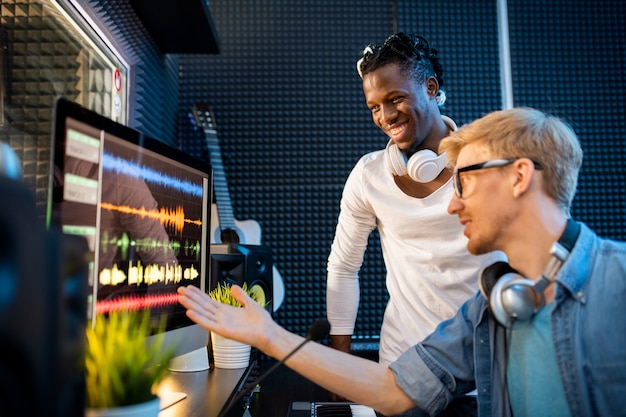 Jeune musicien ou producteur montrant un groupe d'homme africain de formes d'ondes sonores sur écran d'ordinateur tout en travaillant en équipe