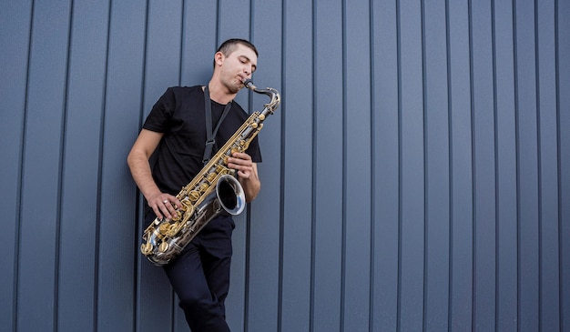 Jeune musicien de rue jouant du saxophone près du grand mur bleu